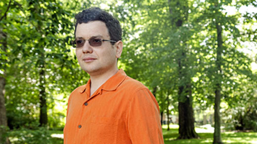 Mark Braverman, in an orange shirt, stands on a path lined with trees.