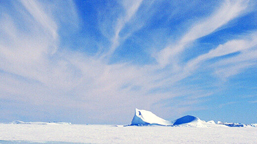 Photograph showing cirrus clouds in a blue sky above an expanse of flat, snow-covered ice.