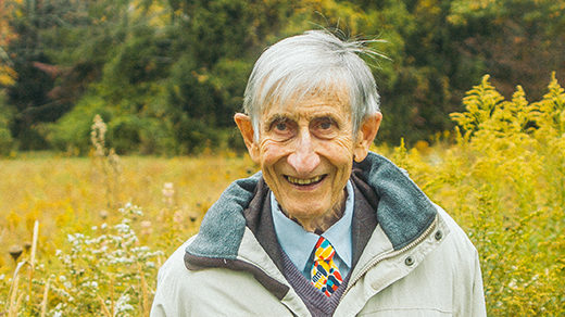 Photo of Freeman Dyson standing in a meadow in front of a forest