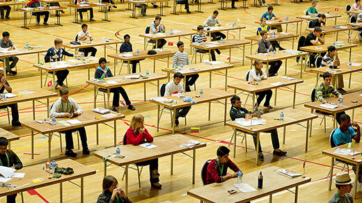 Photo of students sitting at desks competing in the International Mathematical Olympiad