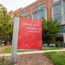 A red sign that reads “Clinical Center, Building 10” outside of a brick building