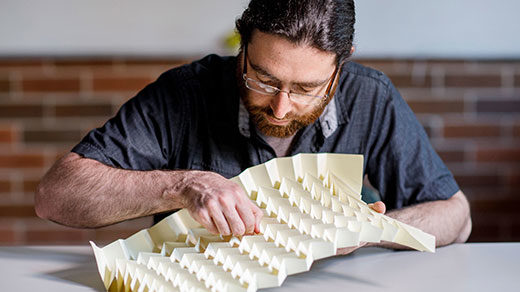 Michael Assis folding a large, beige sheet or Miura-ori