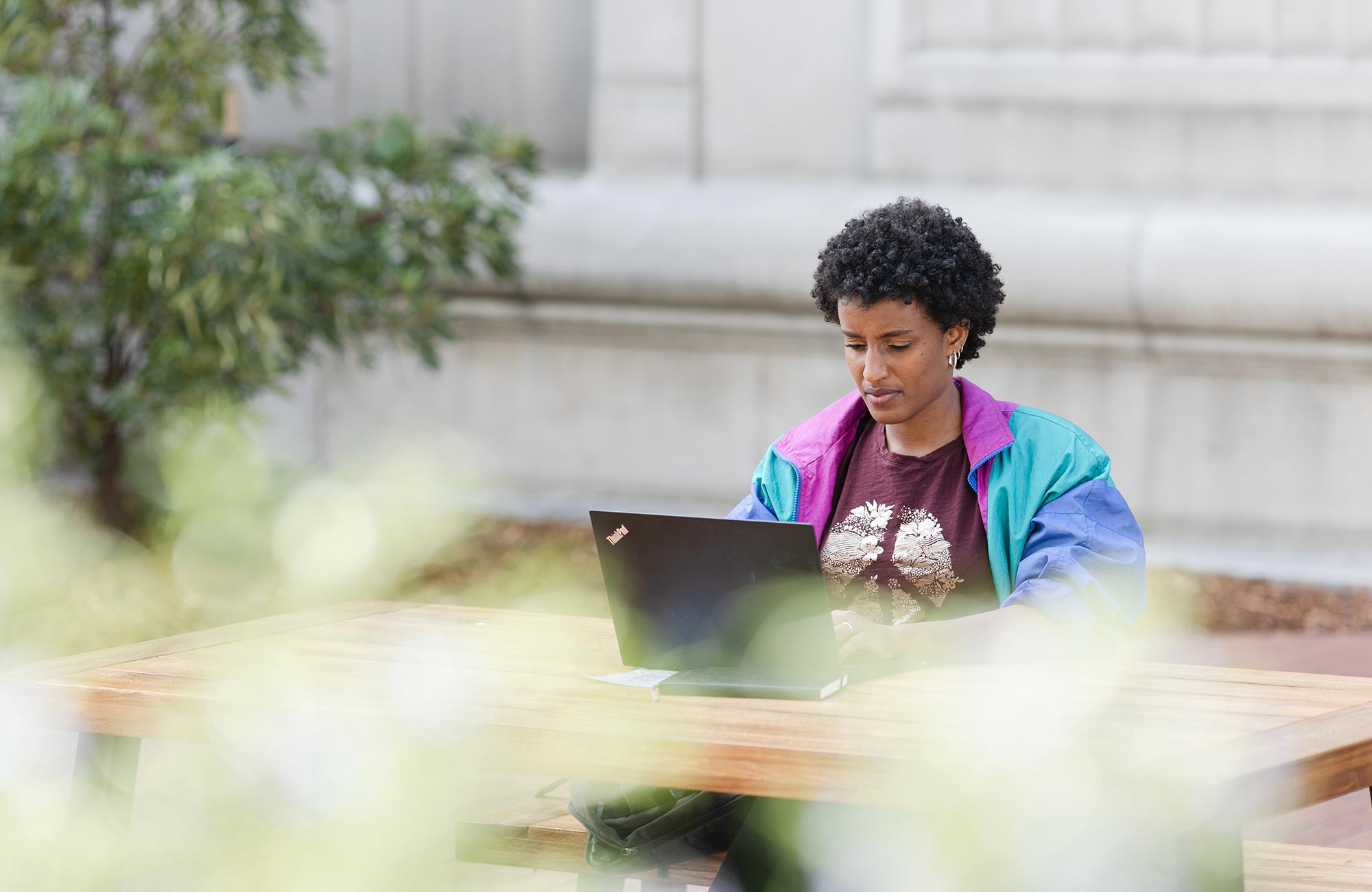 A diptych. On the left, Rediet Abebe sitting outside working on a laptop. On the right, a close-up of Abebe's laptop screen showing an article on increasing the presence of Black people in the field of artificial intelligence.