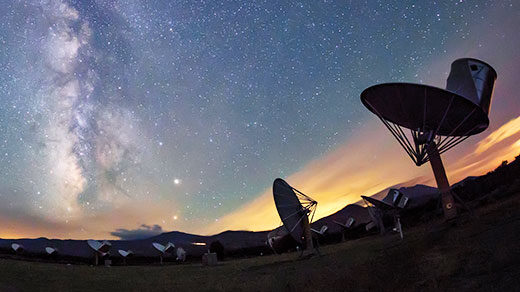 Photo of radio telescopes at the Allen Telescope Array with a starry sky featuring the Milky Way in the background.