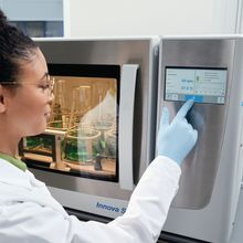 Woman in a labcoat and gloves pushing a button on the Eppendorf VisioNize system